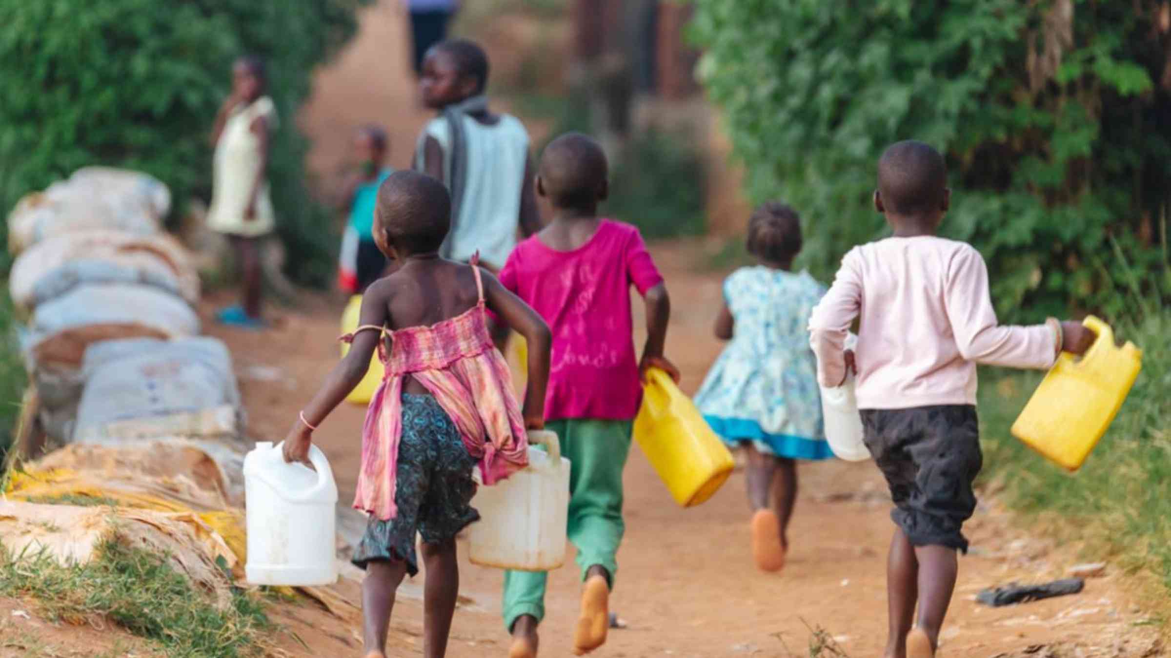 Children carry jugs of water on a dirt road