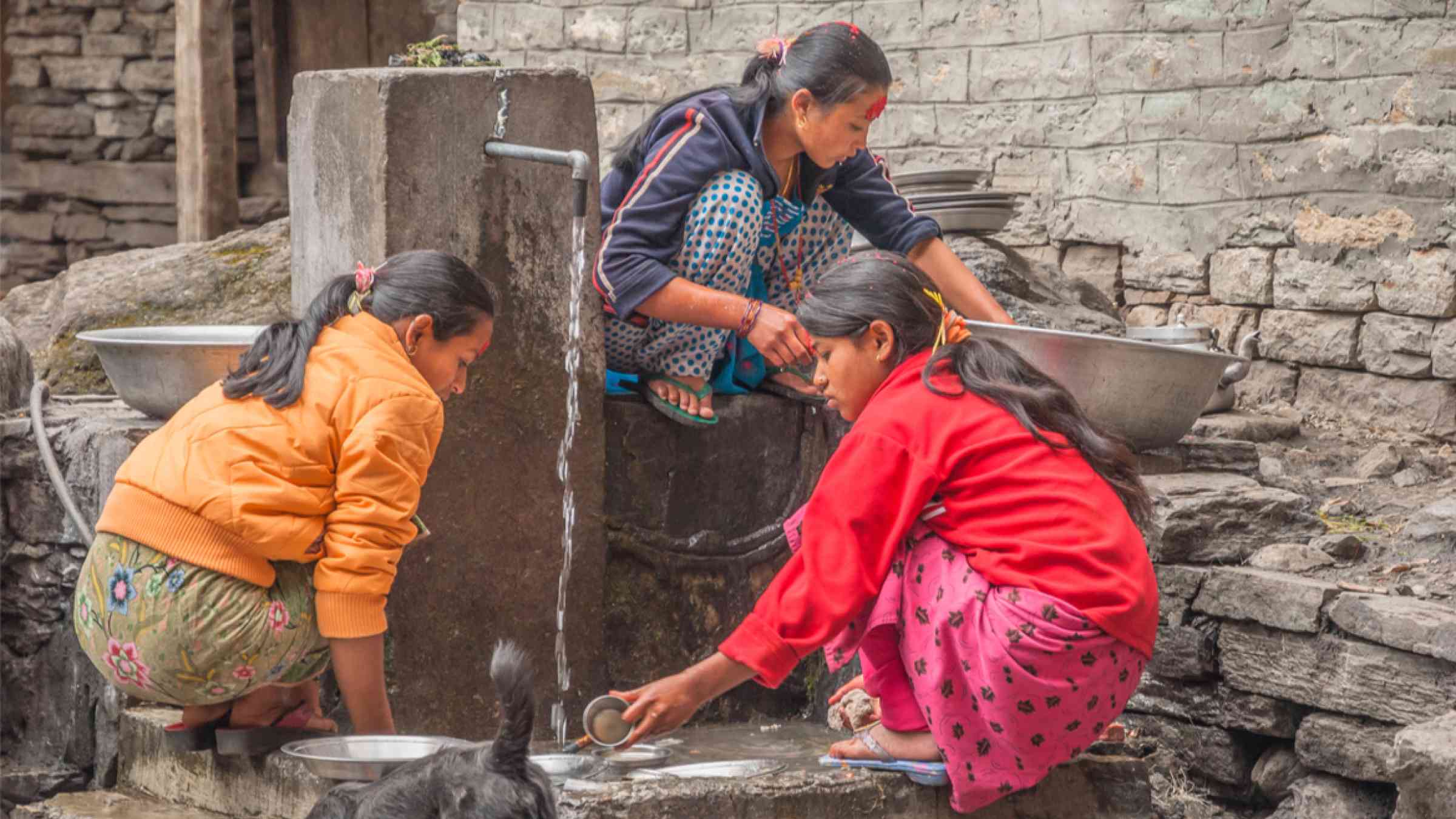 Two young women and a girl are busy washing dishes in the street of a village in Nepal