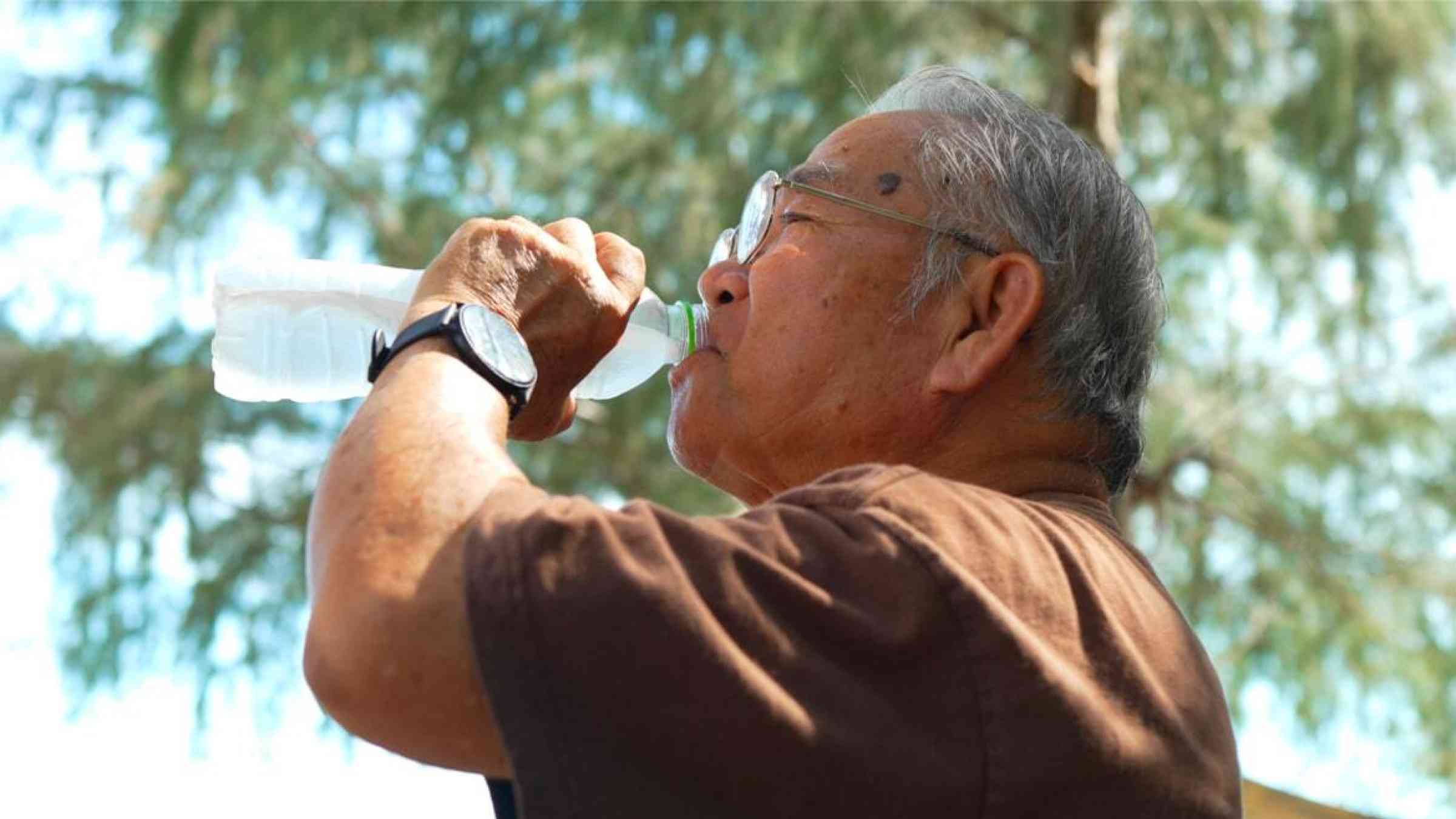 An elderly man drinks from a water bottle on a hot day