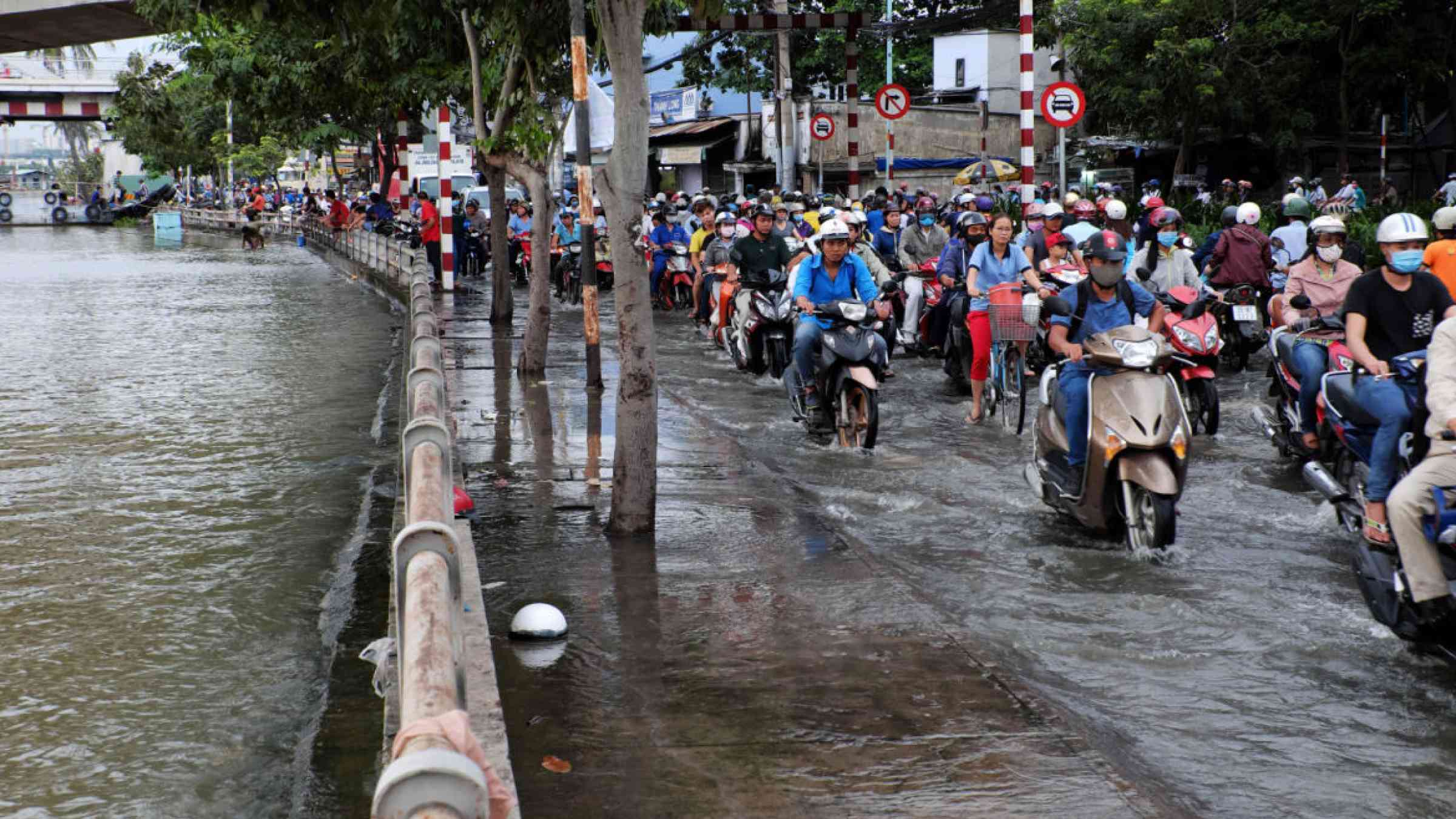 People ride their motorcycle in a flooded street in Ho Chi Minh City