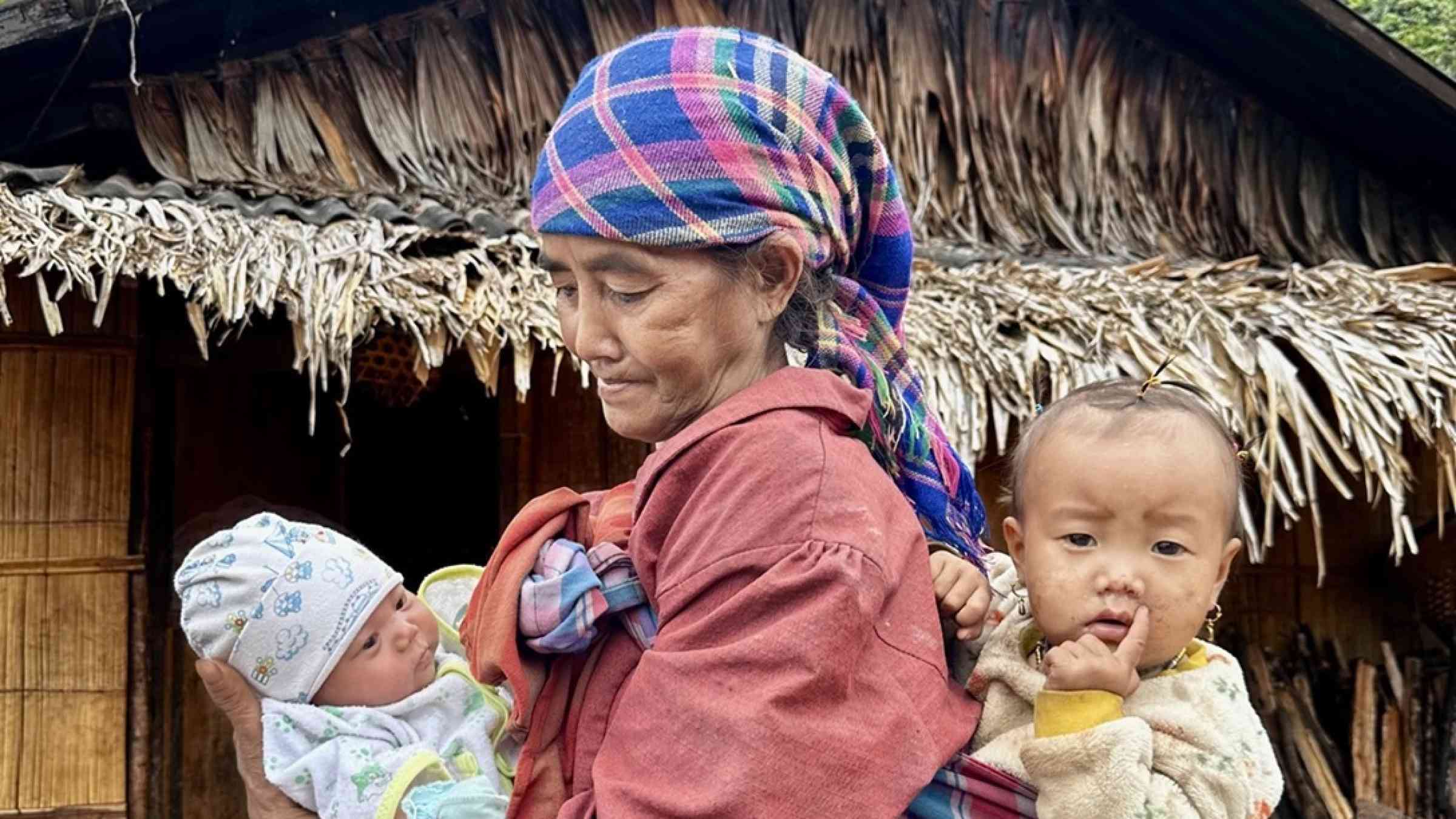 Woman holding two children in a Laotian village