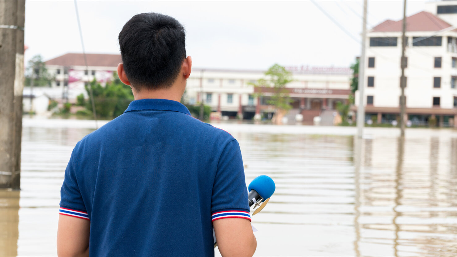 Reporter holding microphone interview in a heavy flooding situation in Sakon Nakhon, Thailand.