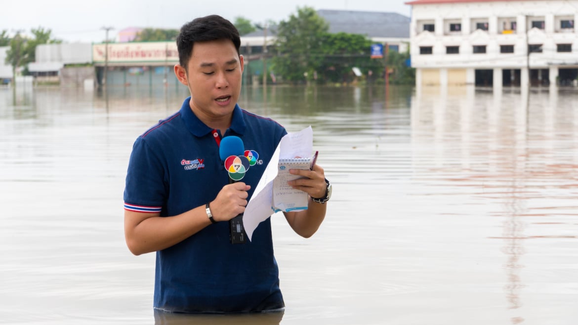 Reporter holding microphone interview in a heavy flooding situation in Sakon Nakhon, Thailand.