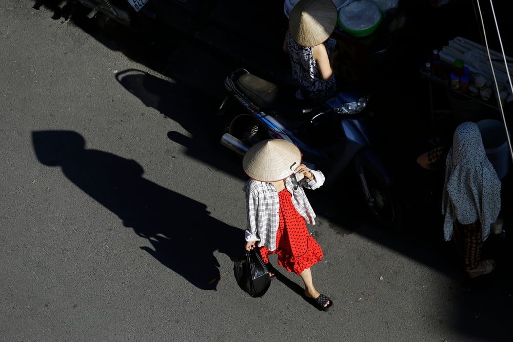 A woman shields herself from the sun on a city street in Vietnam