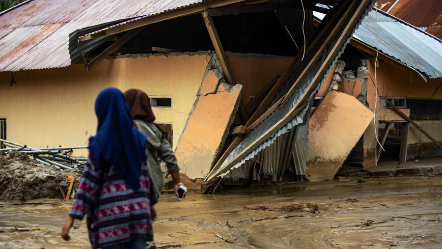 Photo: Girls walk past the destroyed health center in Banga Bagit in Indonesia after extreme storms and floods left thousands displaced in 2019. ©UNFPALearson  
