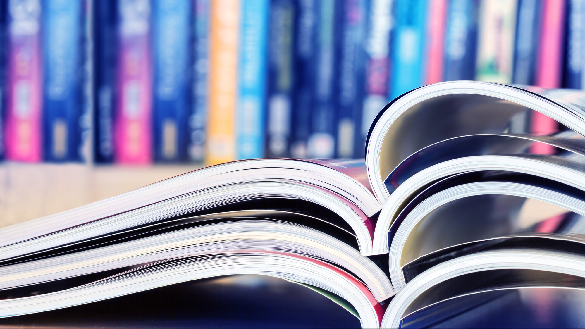 لقطة مقرَّبة لمجلات مفتوحة مكدَّسة مع خلفية رفوف كتب ضبابية