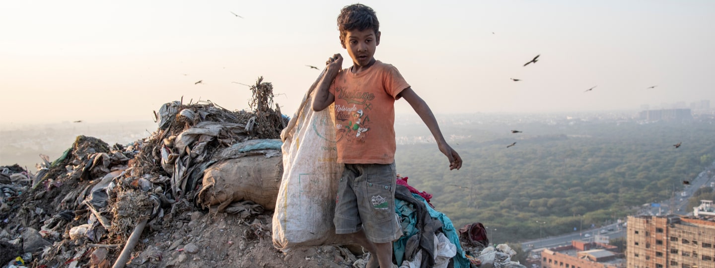 A poor boy collecting garbage waste from a landfill site in the outskirts of Delhi, India.