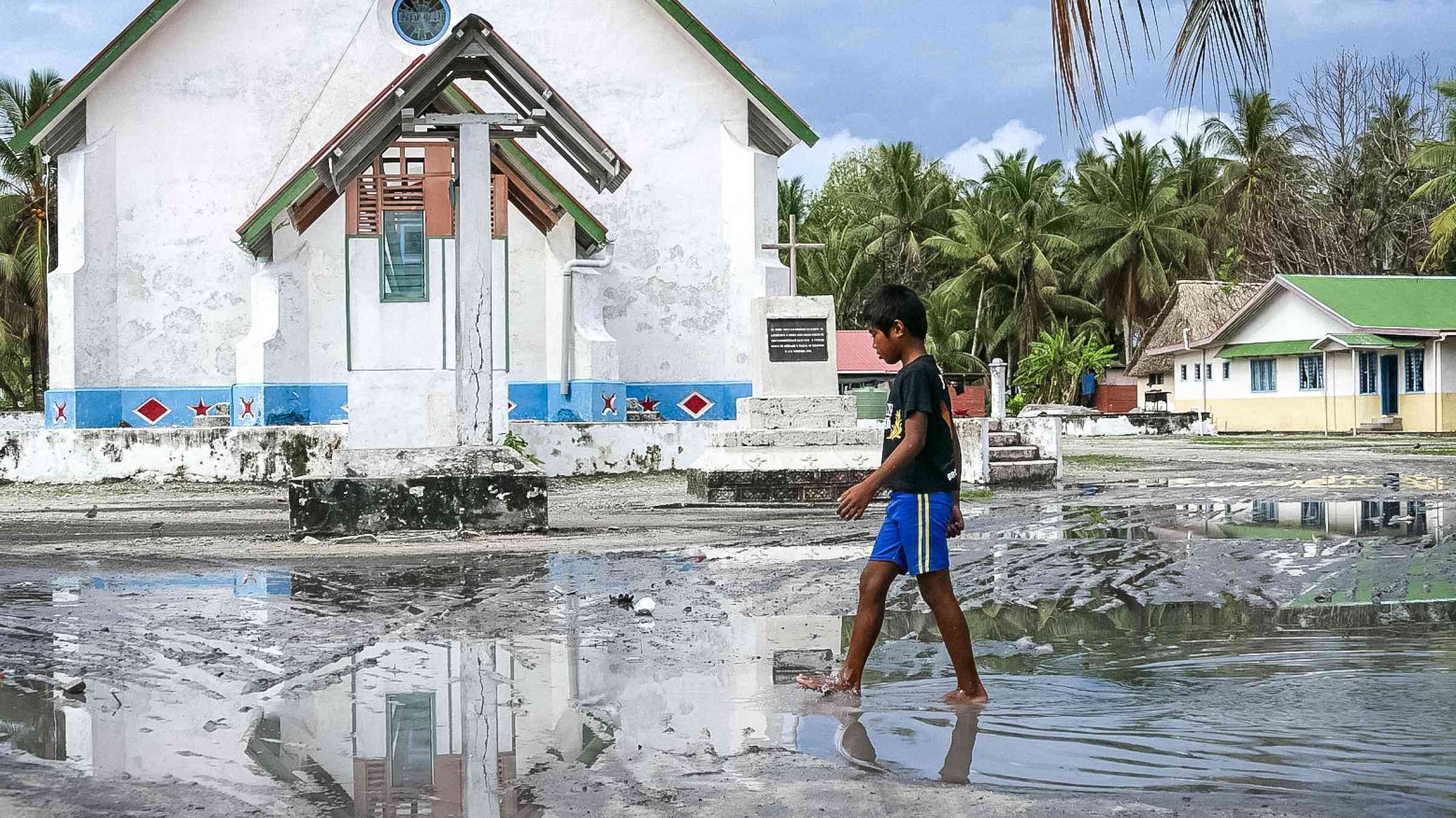 Boy walks through street in Tuvalu after hurricane Pam 2015