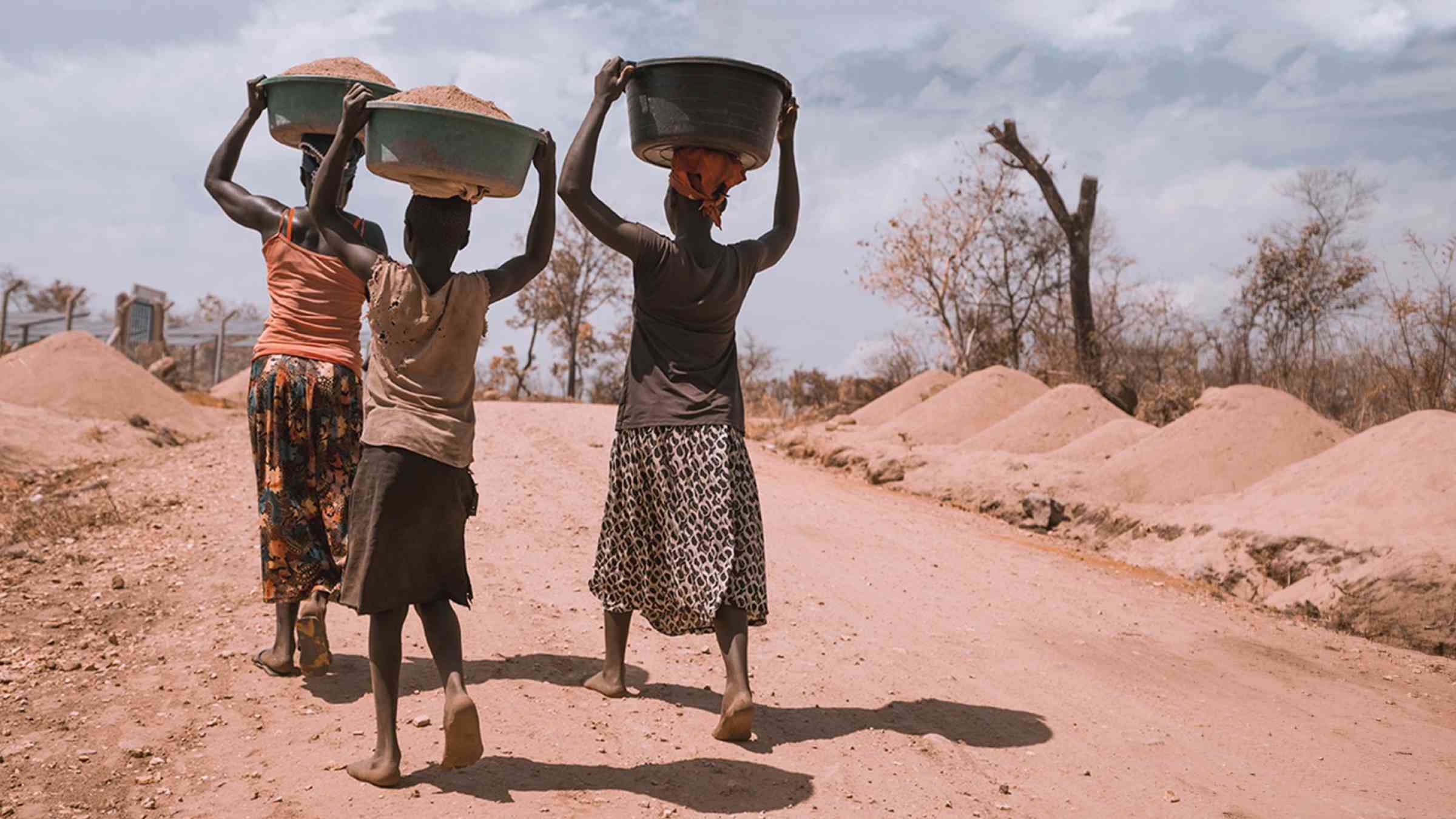 Three women carrying containers walk through a dry area in Uganda