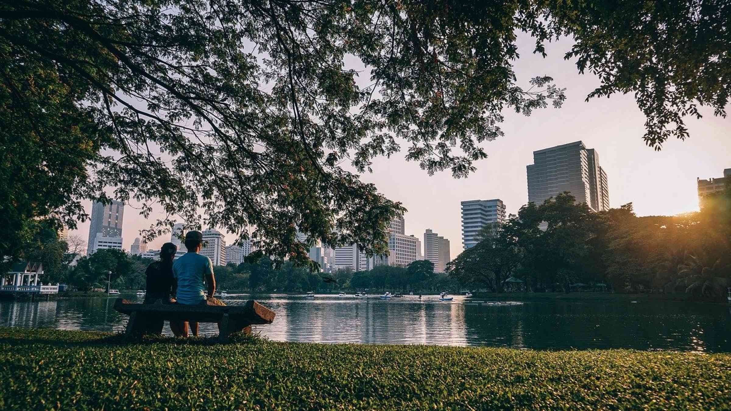 Two people sitting on a bench by a river in Bangkok, Thailand