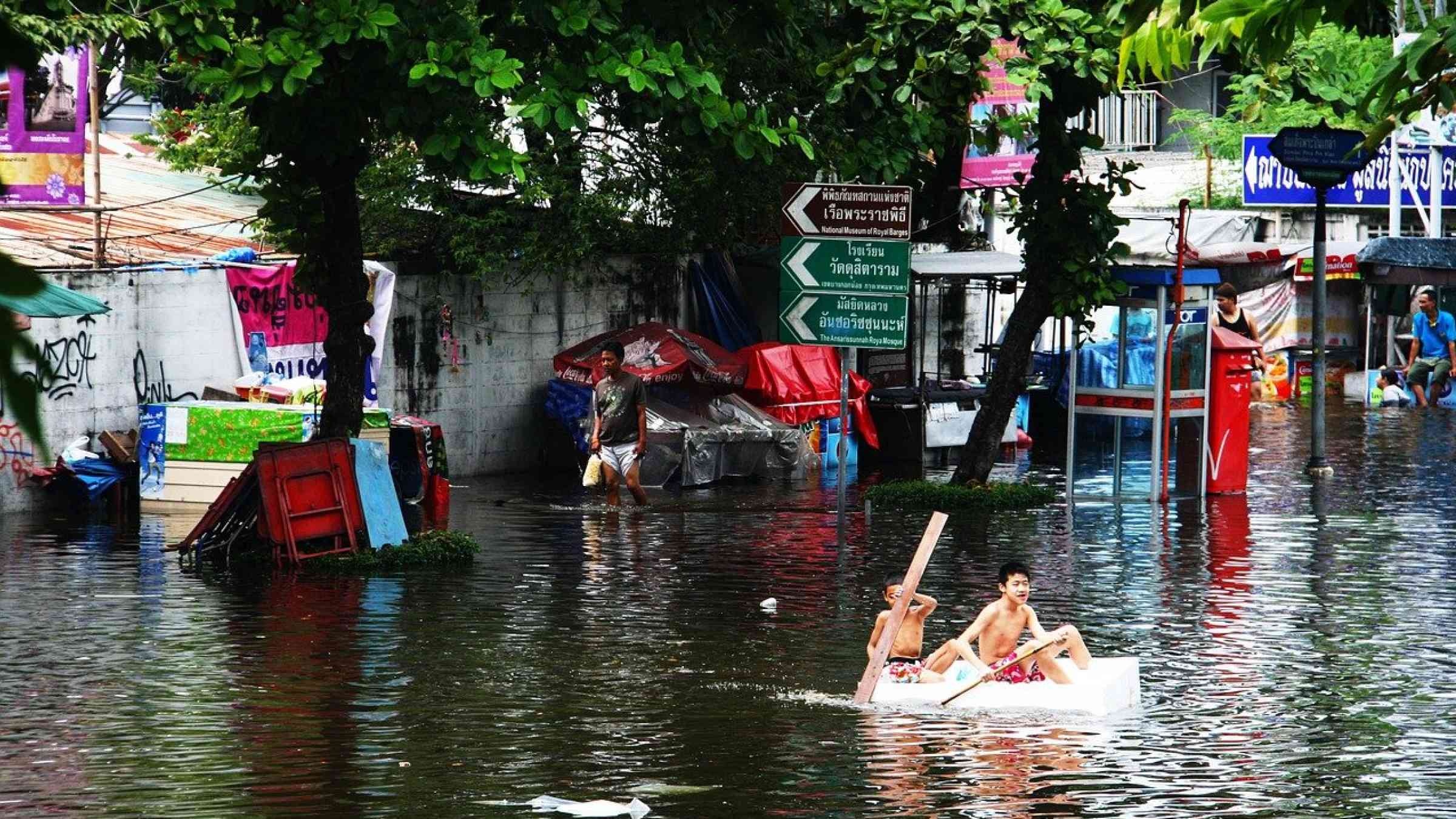 Two boys rowing through flooded waters in a makeshift boat