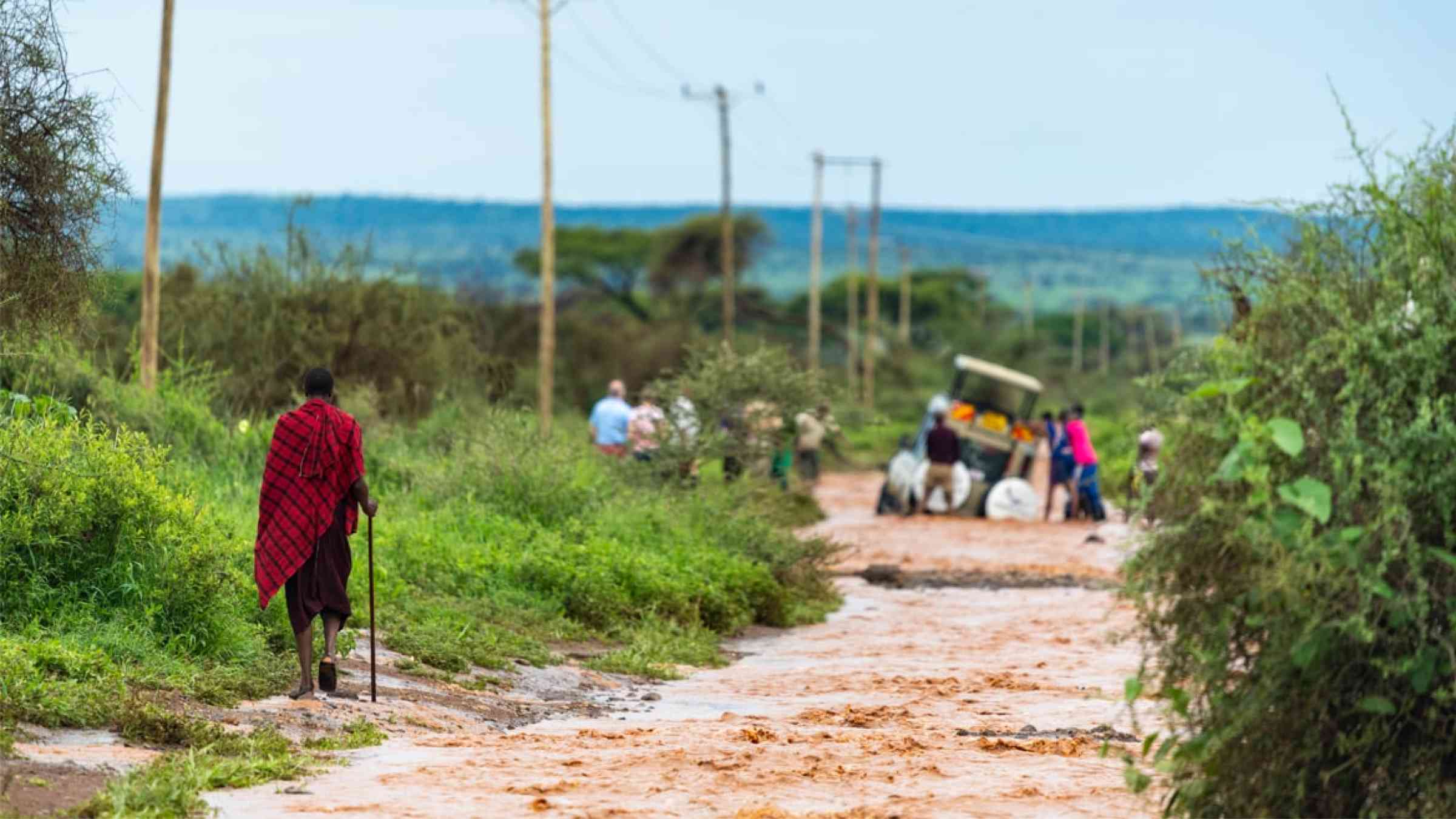 Masai warrior walking beside flooded dirt road, Amboseli NP, Kenya.
