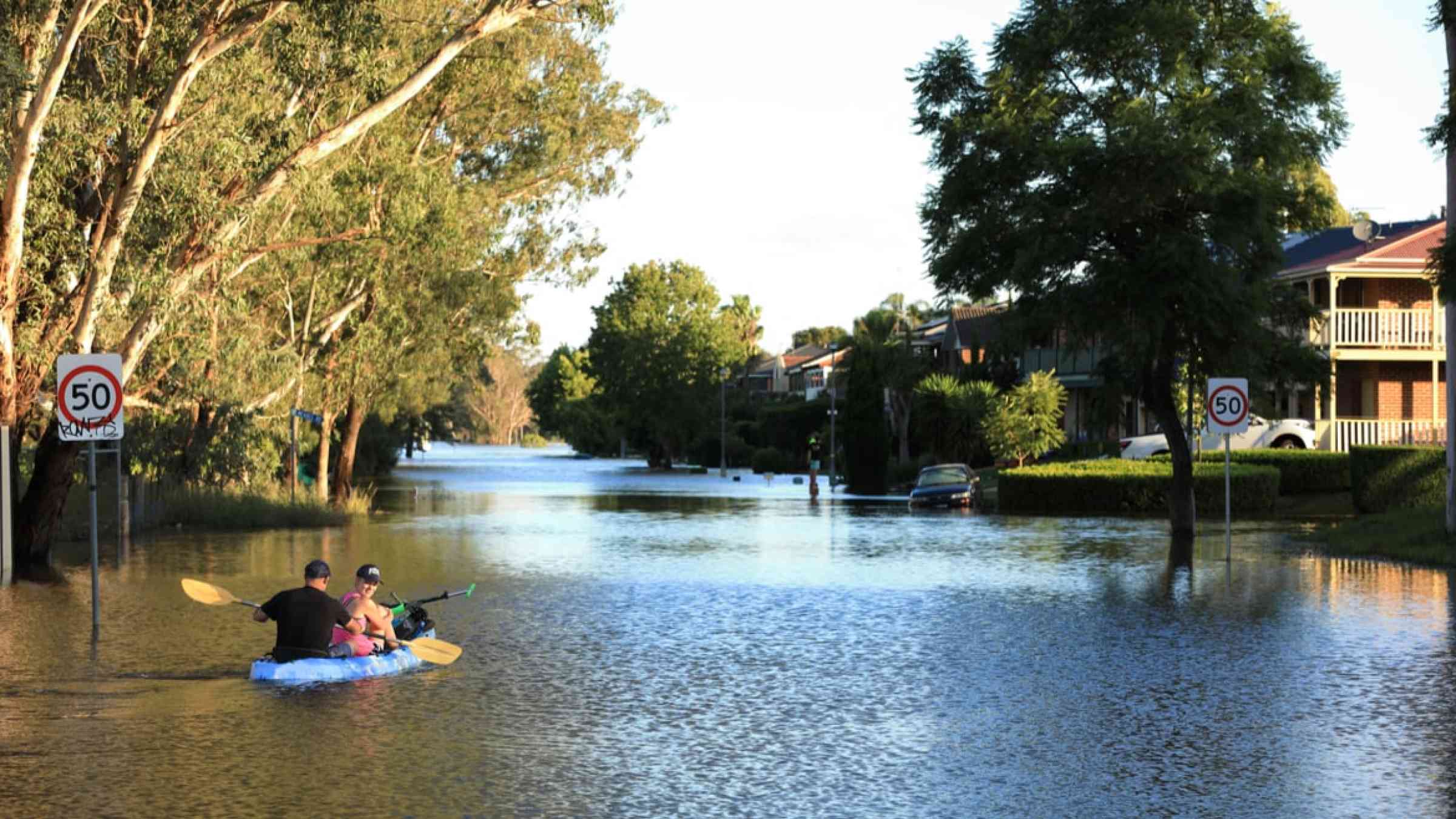 A man and a woman use a kayak to travel up a flooded street in McGraths Hill, Australia (2021)