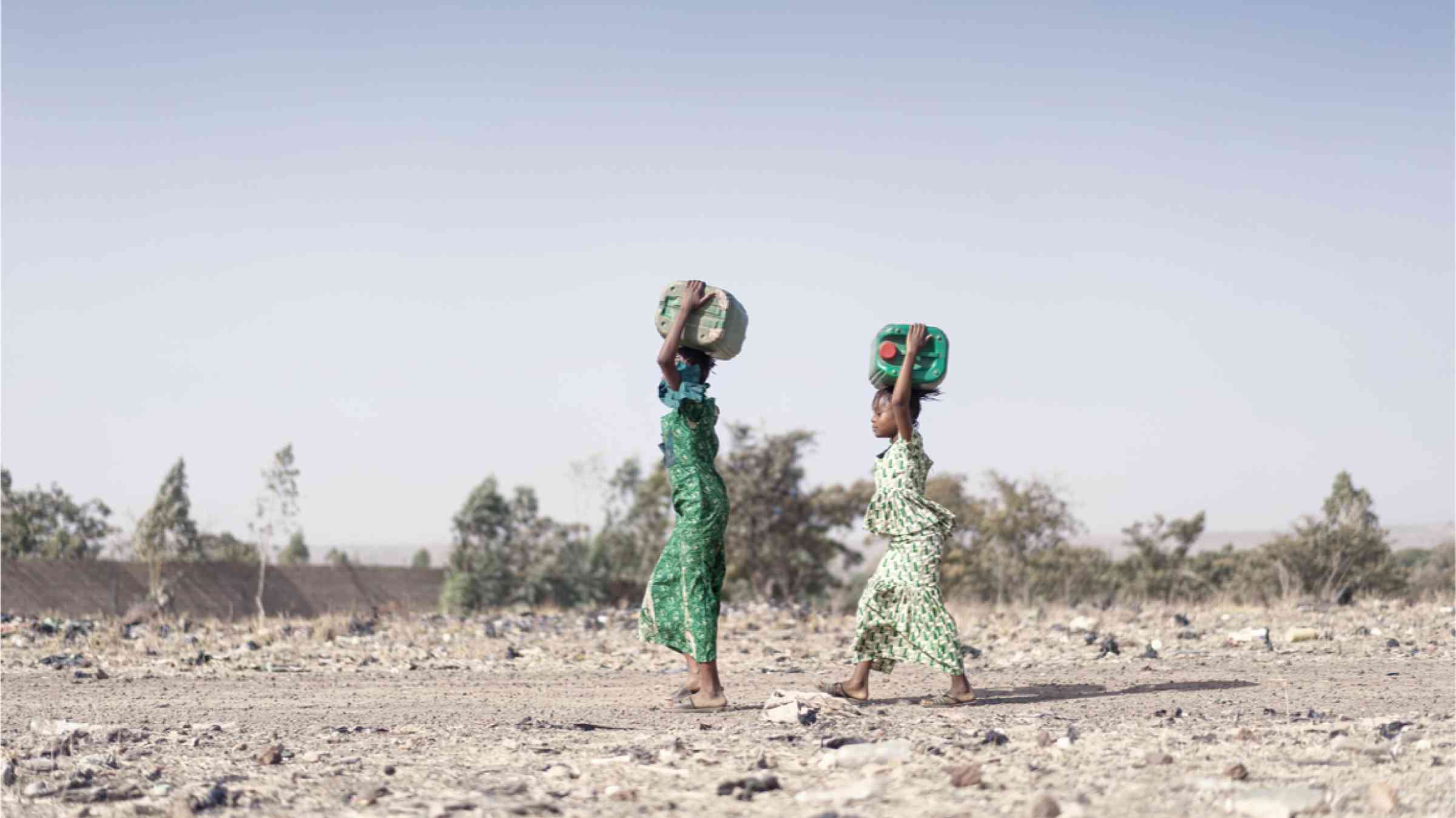 African ethnicity carrying water through a desert landscape