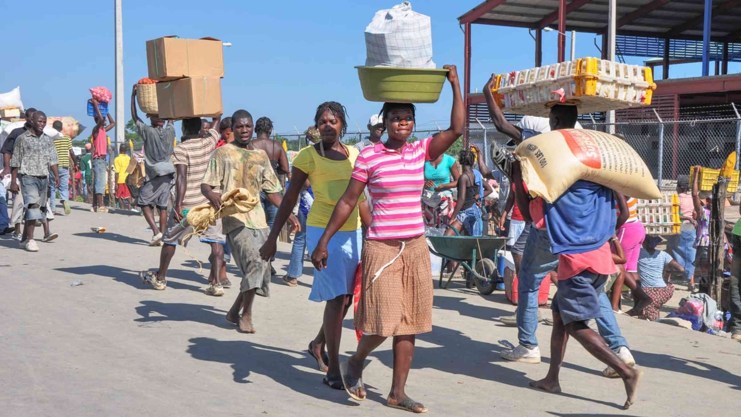 Haitian woman carries a bucket of goods on her head at a Haitian market