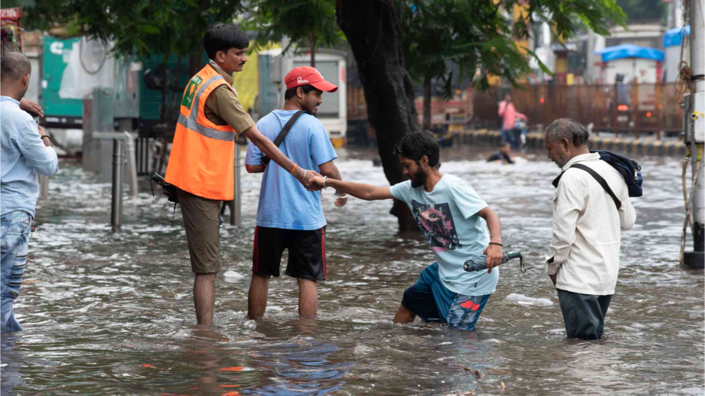 A municipal worker helps pedestrians cross flooded streets after heavy rains in Mumbai, India