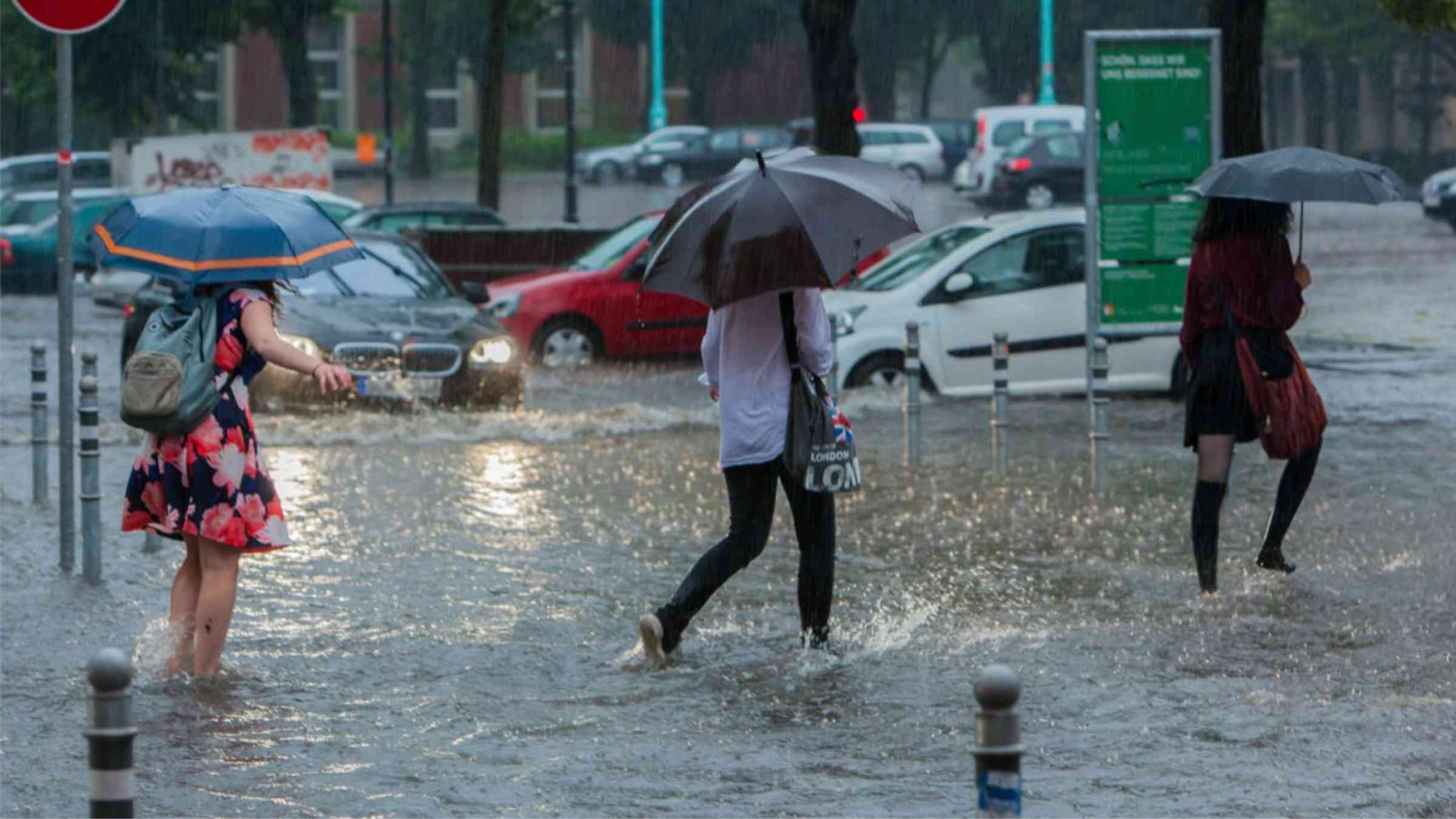 Three women with umbrellas walking through water in floode streets, Berlin, Germany (2017)