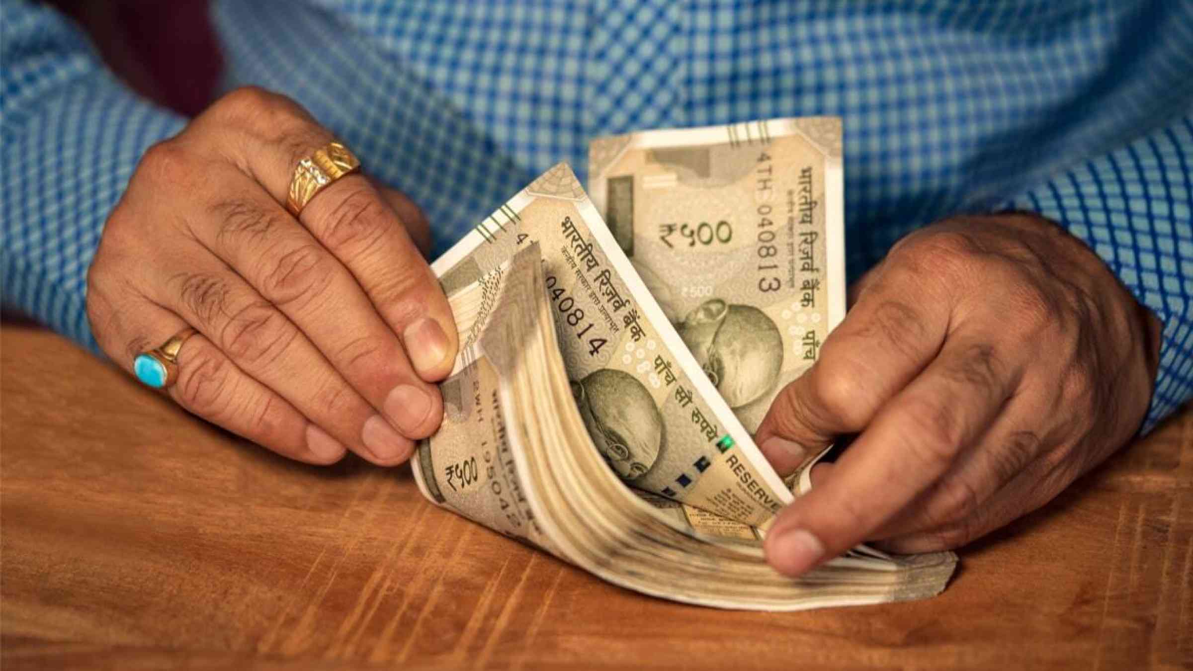 An Indian man counts a stack of five hundred rupees on a wooden table