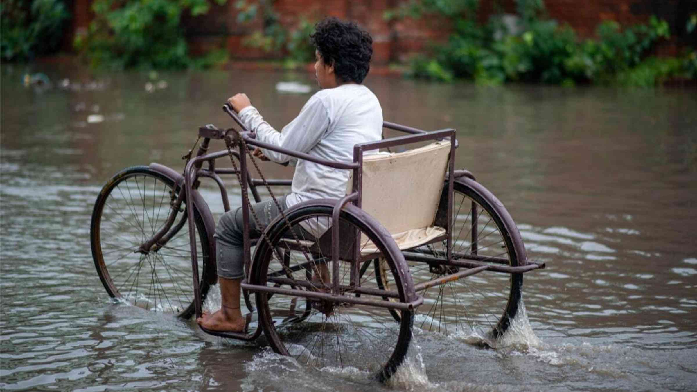 A man uses a modified wheelchair to ride above monsoon floods