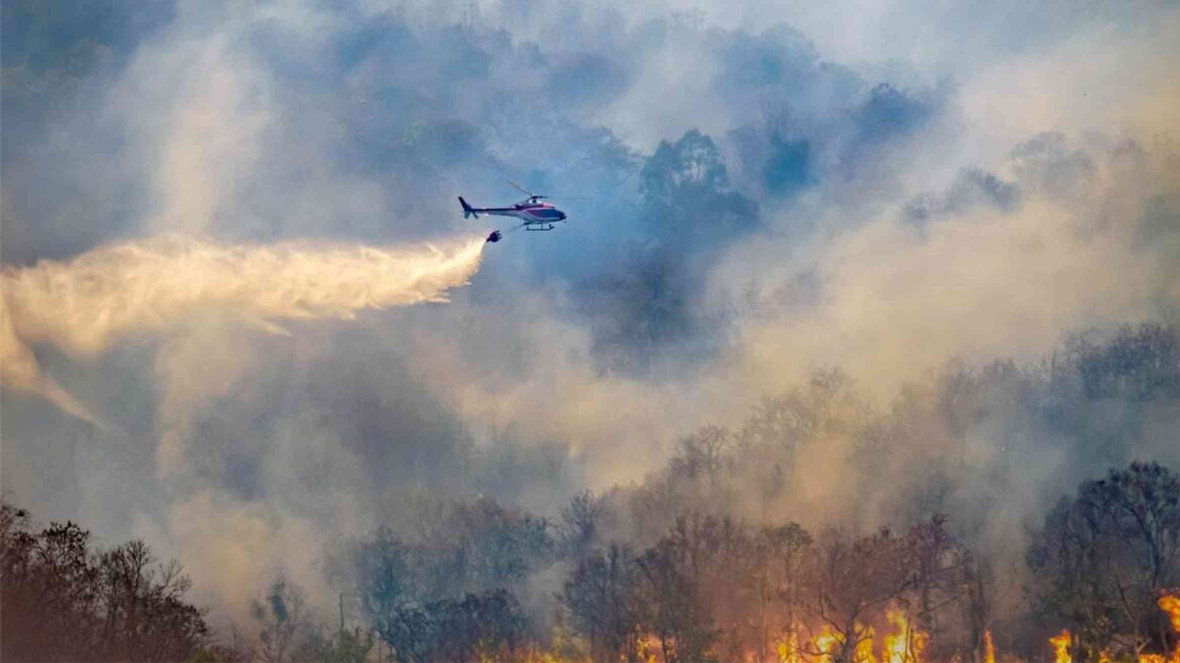 A helicopter drops water on a raging bushfire