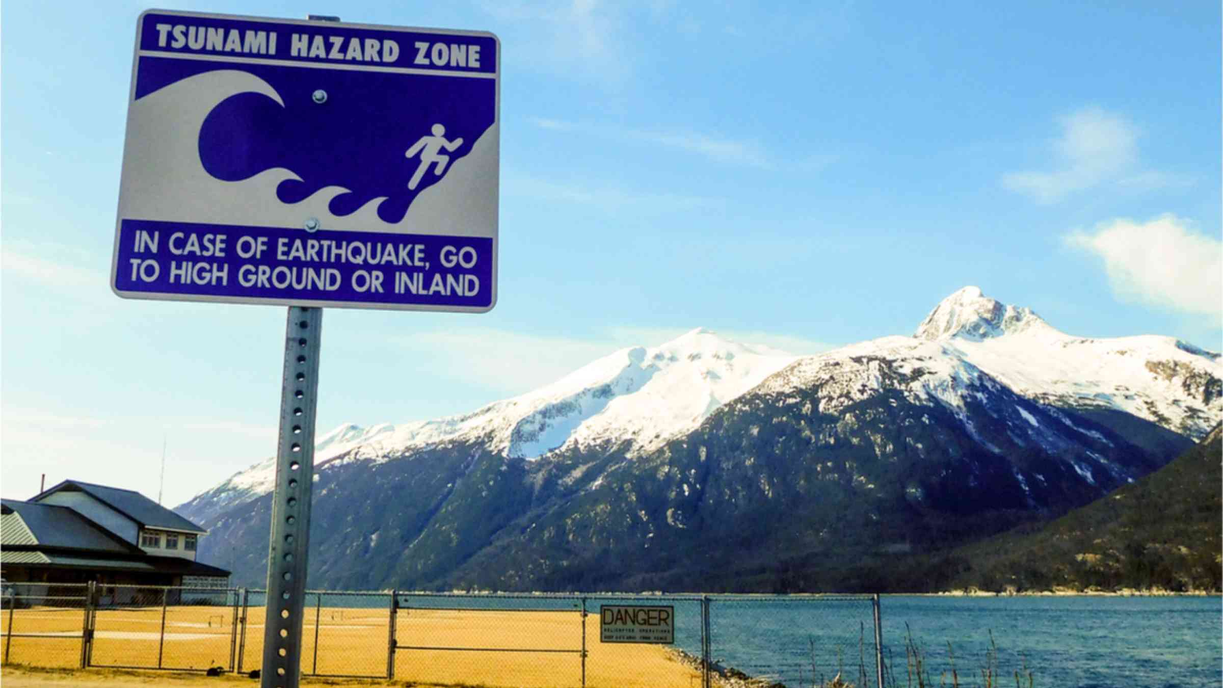 A sign warns of tsunami danger zone in front of coastal mountain region.