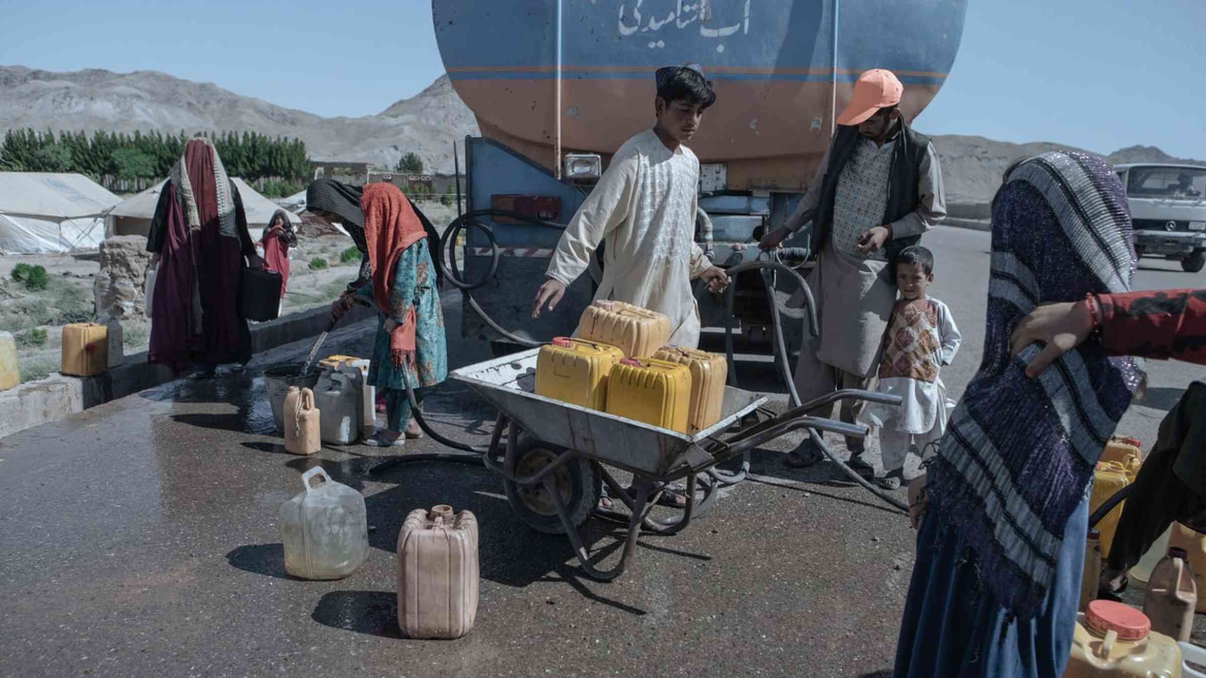 The drought-displaced Afghan children fill water containers to carry to their tents from a tanker at a camp for internally displaced people on the outskirts of Herat province, Afghanistan (2019)