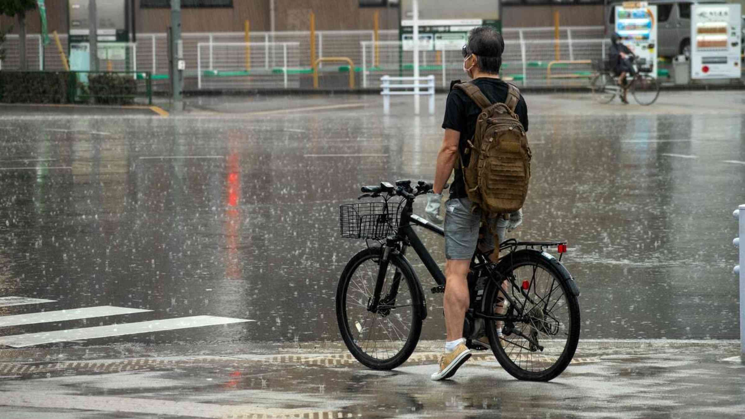 A cyclist waits at a crosswalk under heavy rain in Tokyo