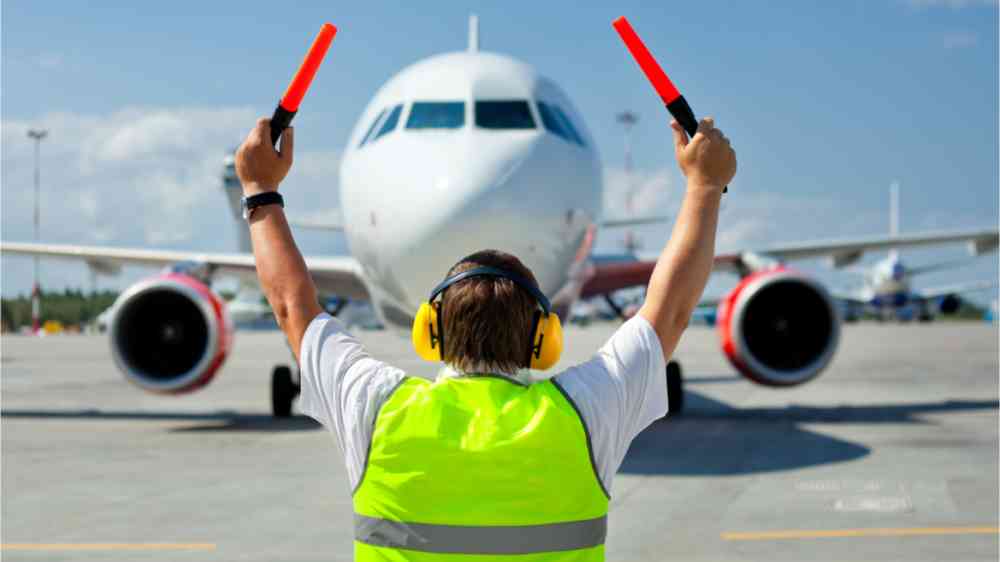 Ground crew in signal vest meets passenger aircraft at the airport. Aircraft moves to the parking lot.