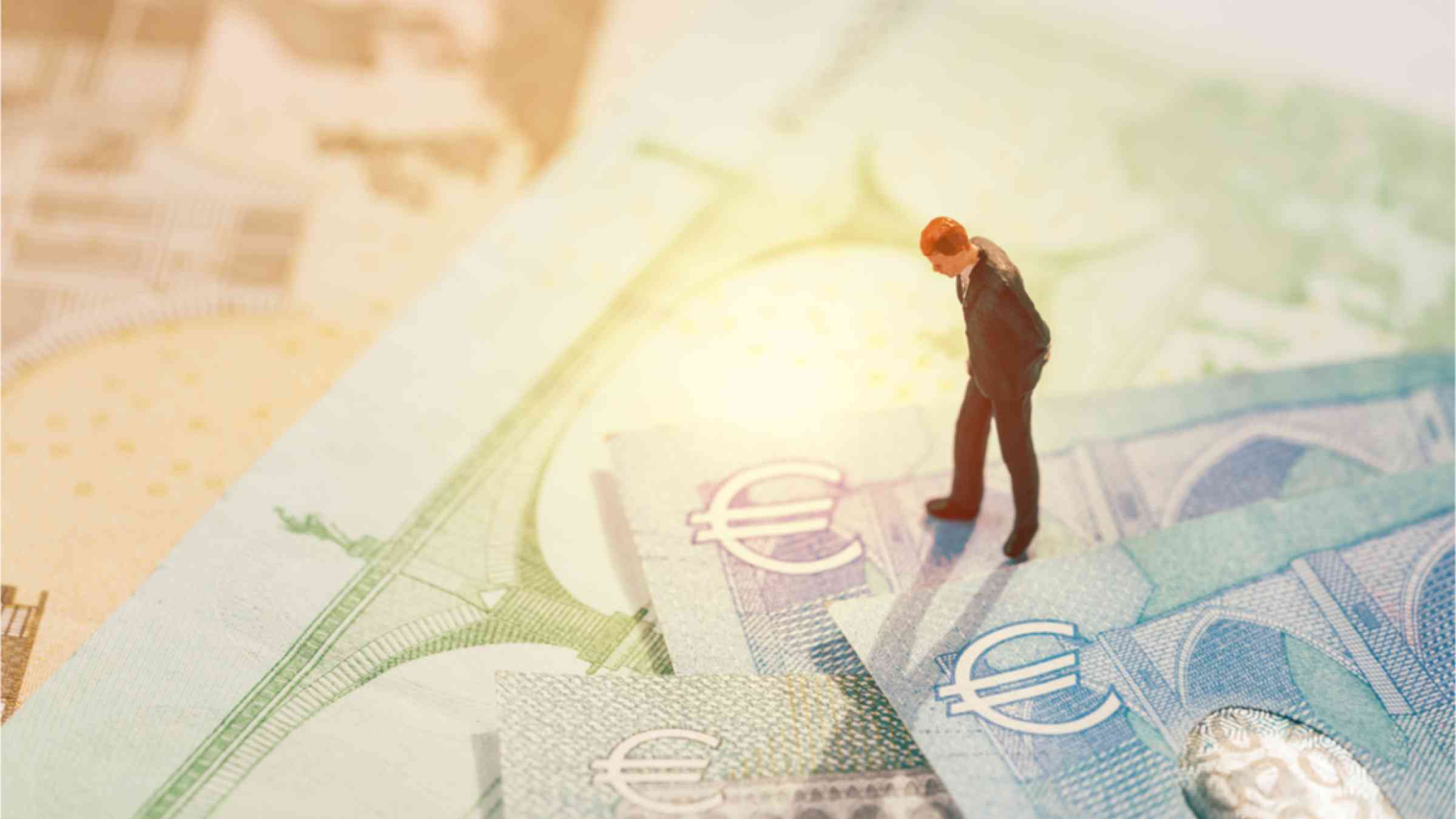 This image shows a mini business man figure looking at euro sign on the stack of banknotes.