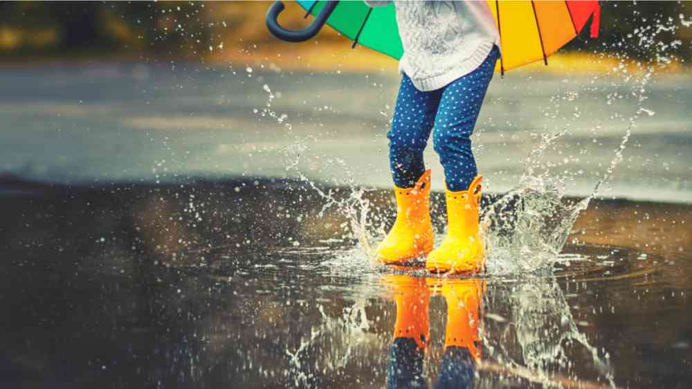 This image shows thefeet of a child in yellow rubber boots jumping into a puddle of rain.
