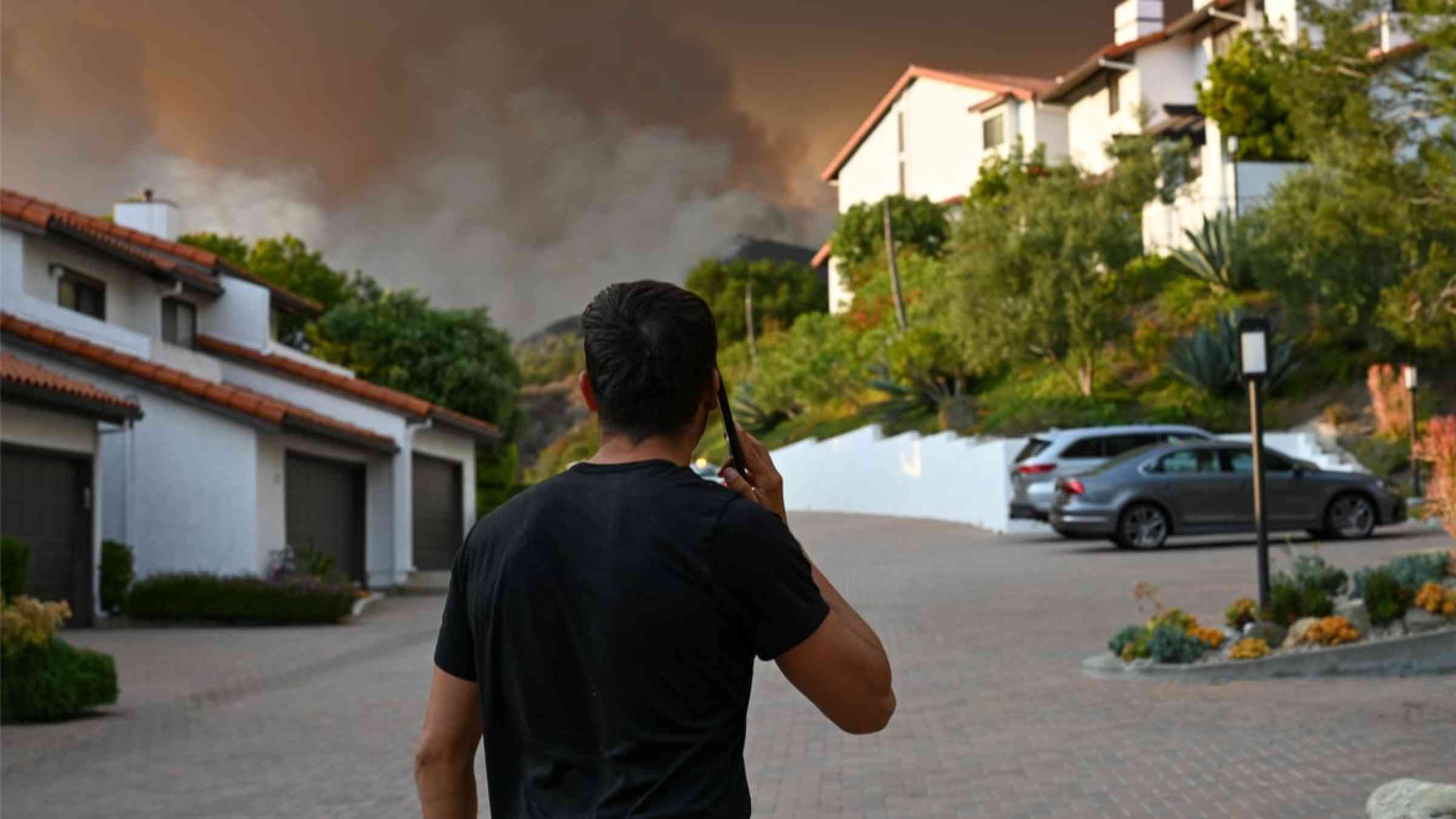 Man on the phone looking at a wildfire in a residential area in California, USA (2021).