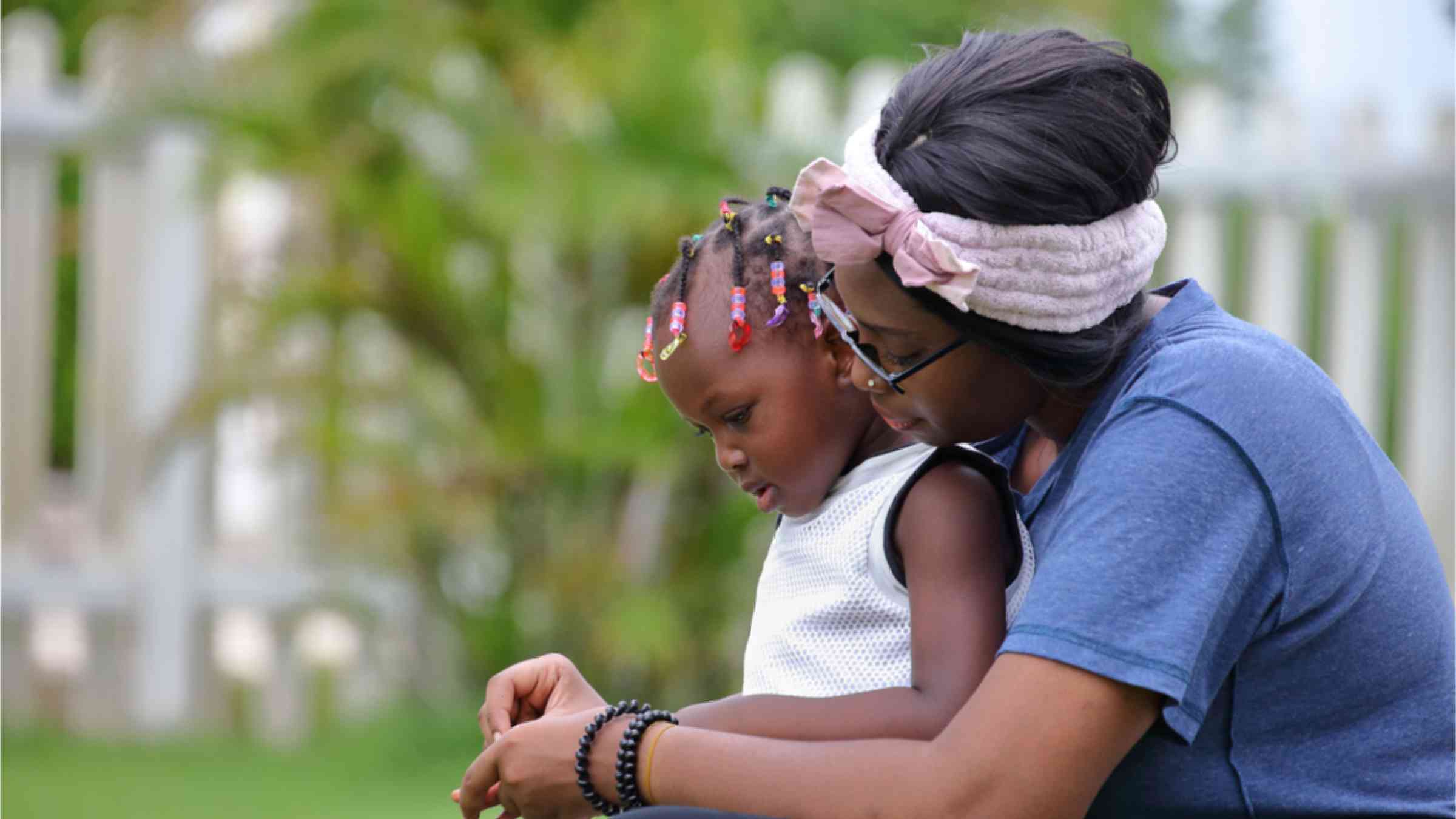 This image shows an African American woman with her daughter outside in the green neighborhood.