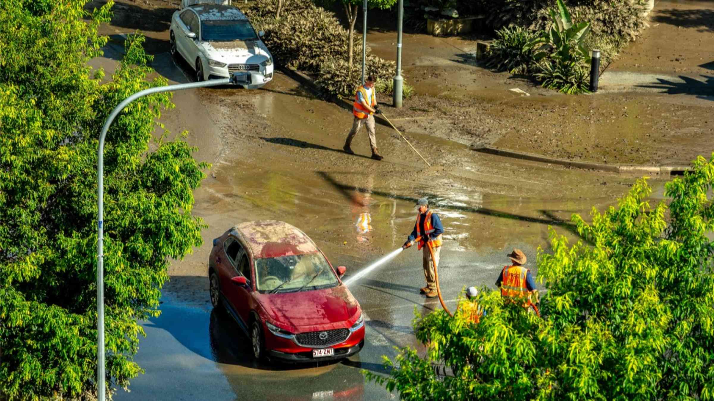 People cleaning up a muddy Brisbane street after the flood event