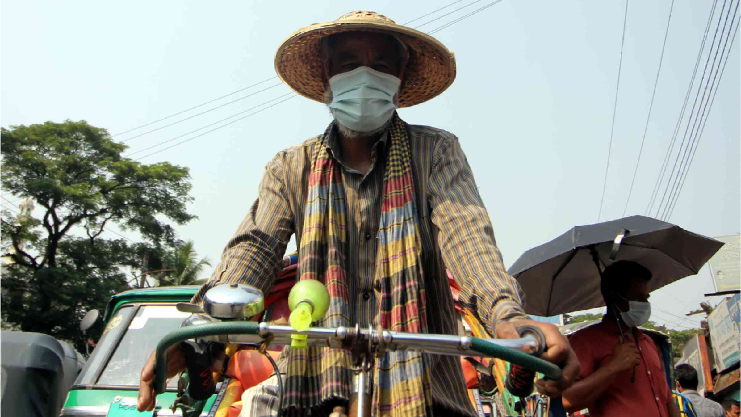 A rickshaw puller wearing an umbrella and a mask in the scorching heat of the summer sun.