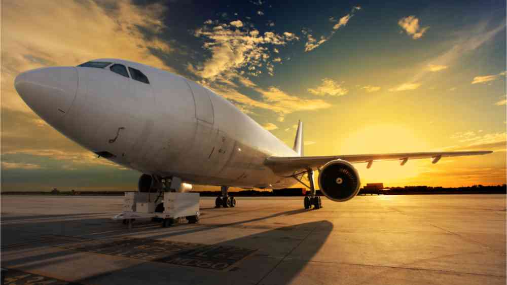 This image shows an airplane in front of the bright yellow rising sun on the runway.