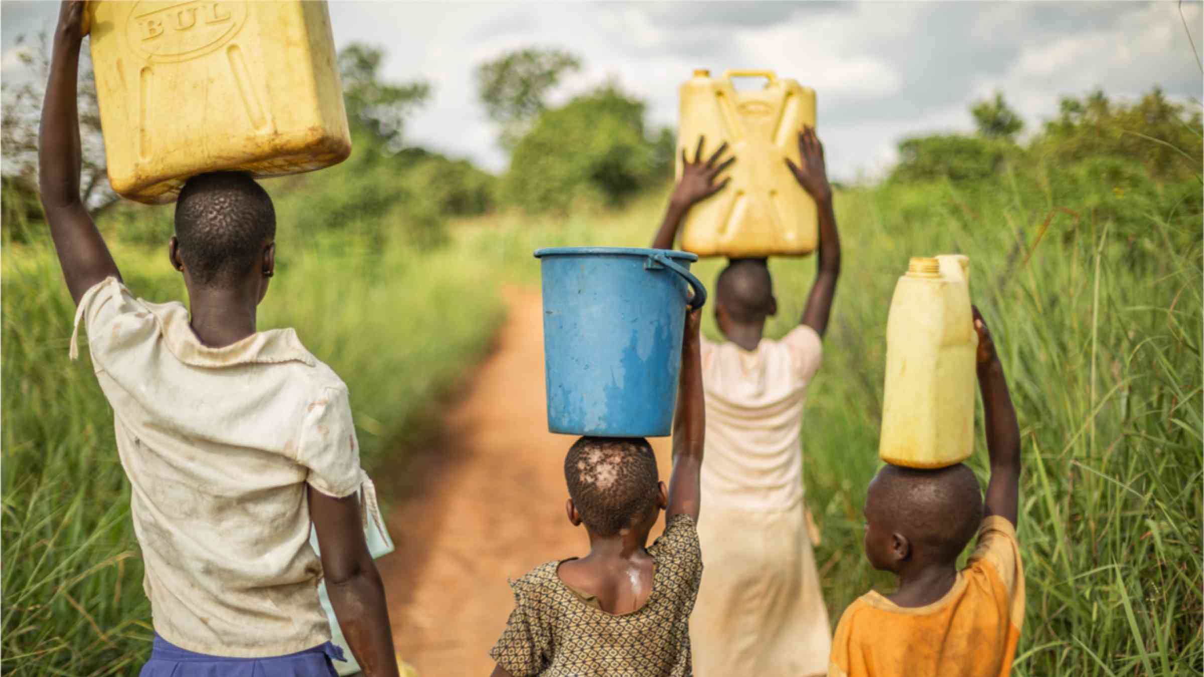 Group of young African children walk with buckets and jerrycans on their heads as they prepare to bring clean water back to their village.