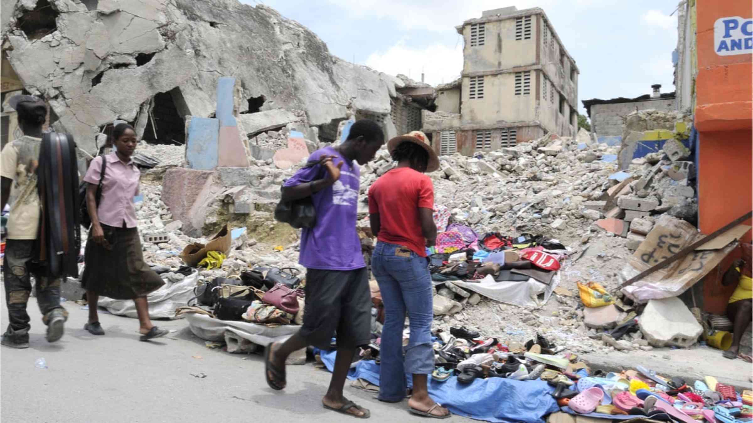 Two people standing in front of a collapsed building after the Haiti earthquake in 2010.