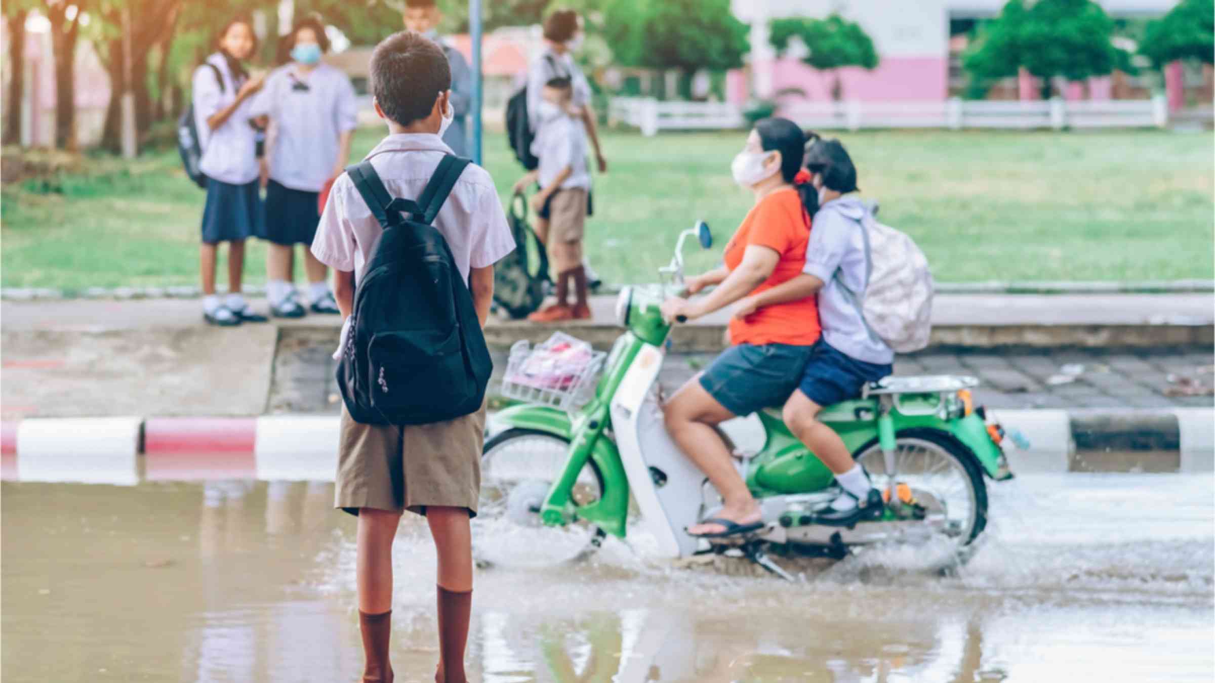 This image shows students wearing masks and a motorcycle driving through flooded streets.