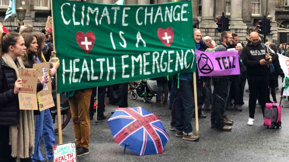 This image shows a group of people demonstrating. They are holding a large green banner that says" Climate change is a health emergency".