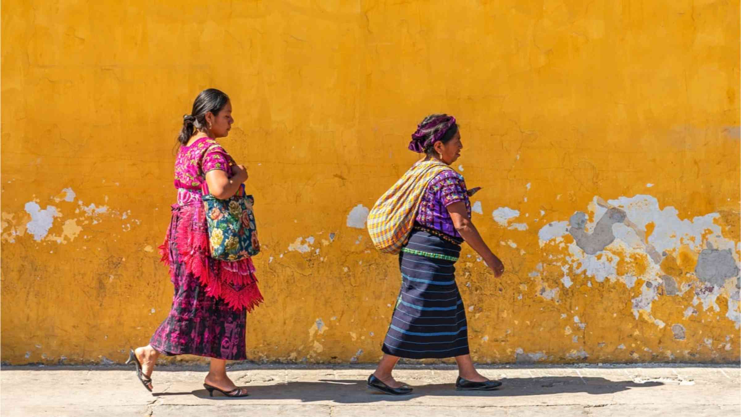Two Mexican women walking in front of a yellow wall.