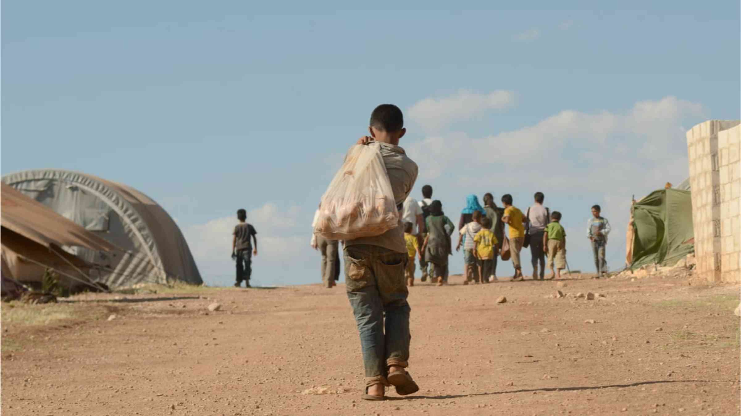 A young boy walking across a refugee camp in Syria.