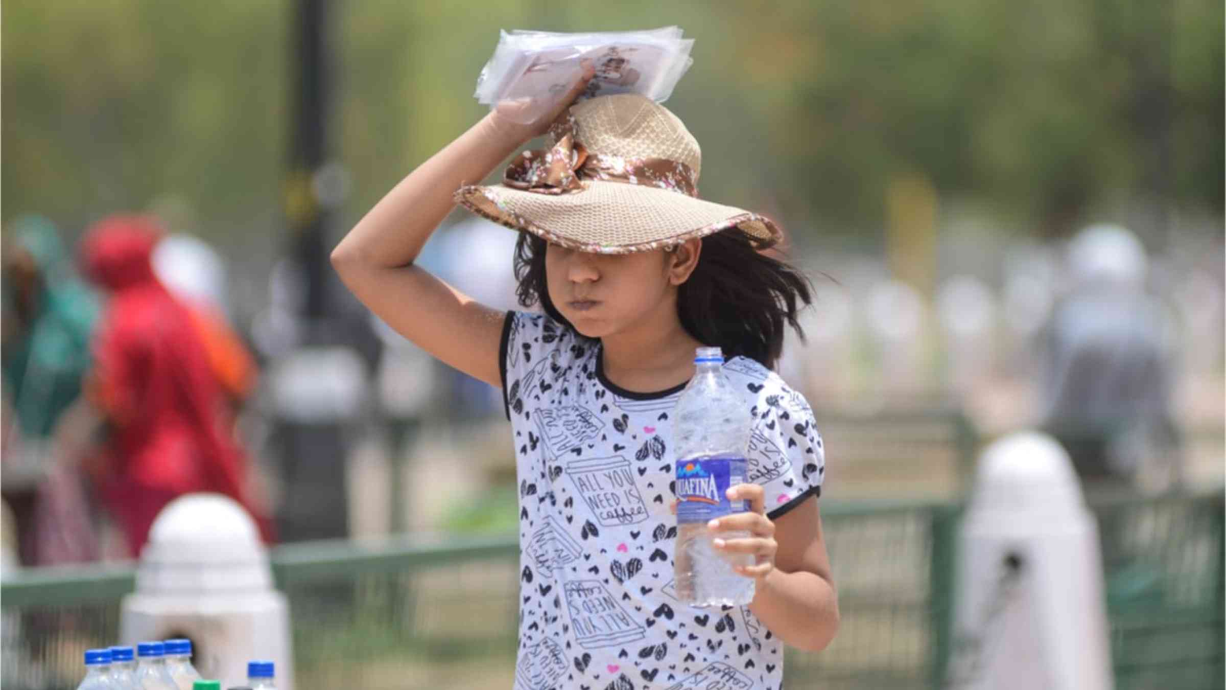 An Indian girl wearing a hat to protect her from the sun and the heat with a bottle of water in her hands.