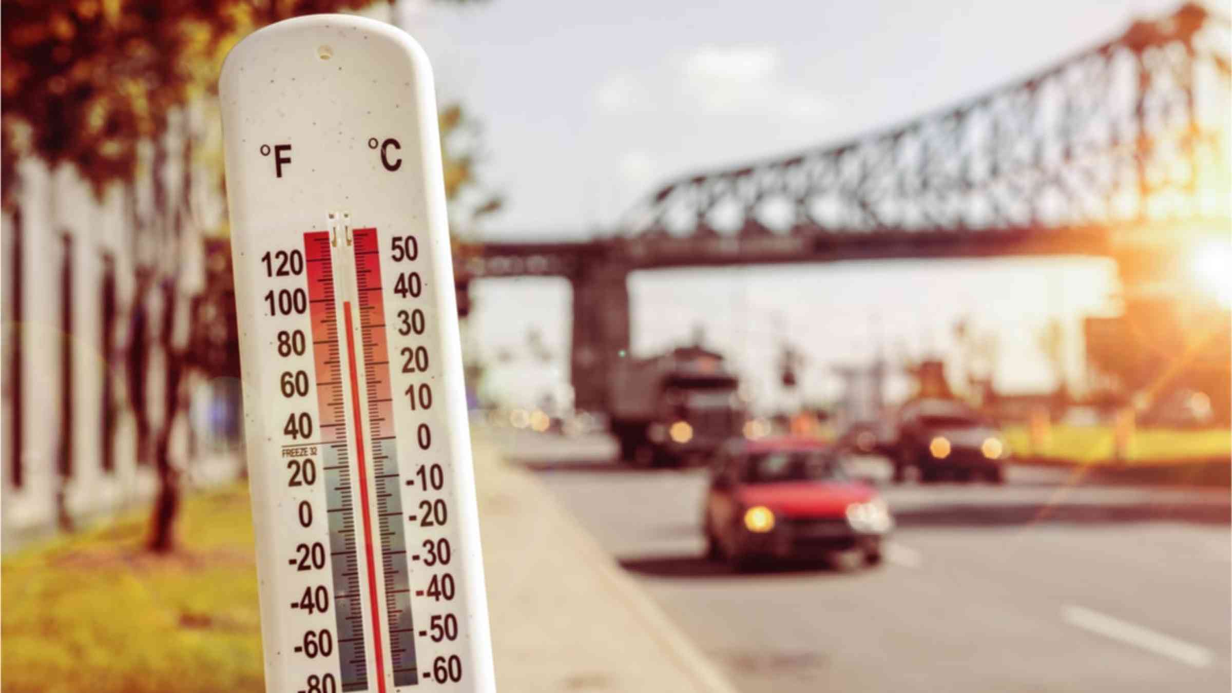 A thermometer showing high temperatures. A city is blurred in the background.