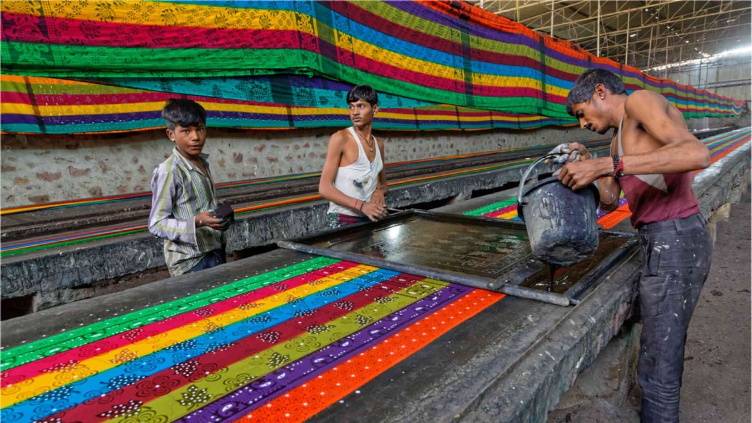 Three men working in a textile factory in India. They are applying print on fabric.