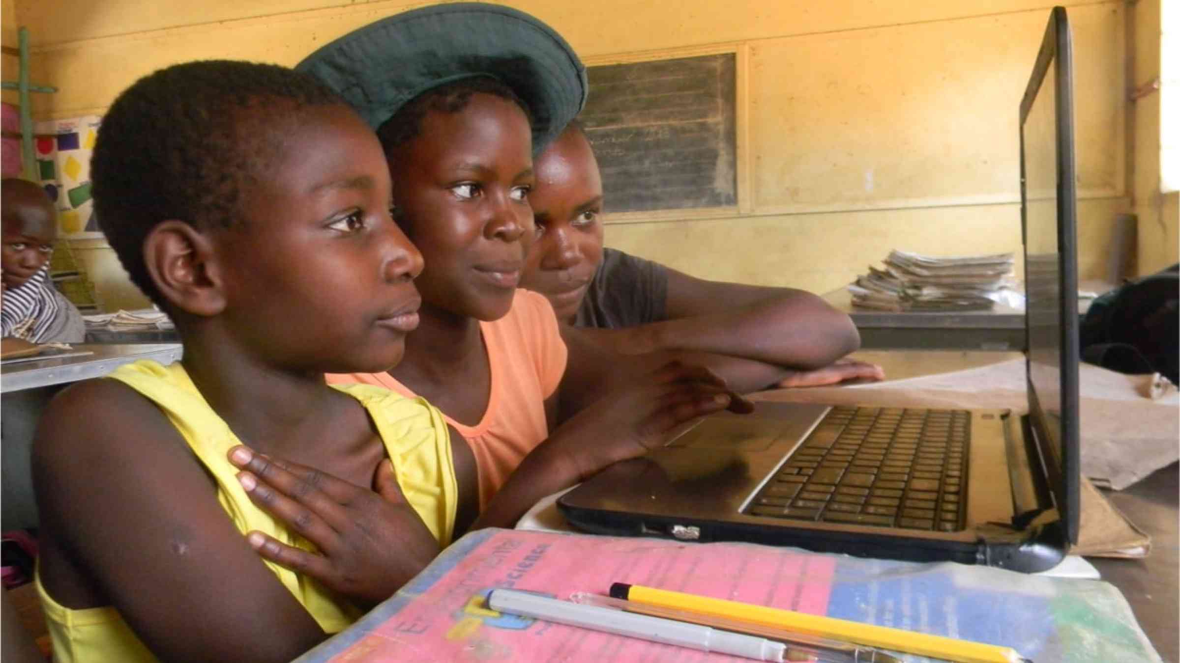 Three high school students in Zimbabwe working on a laptop.