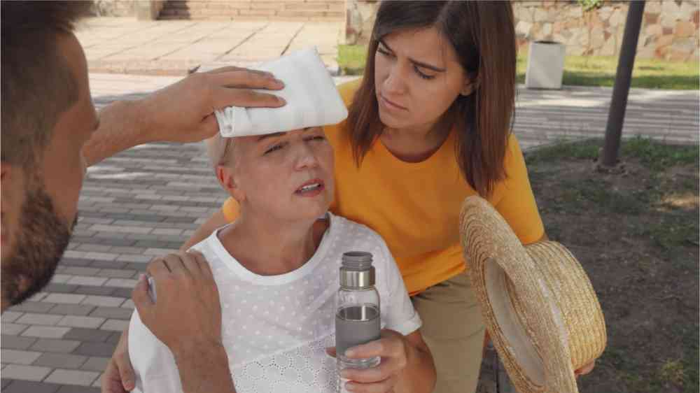 Two people who are helping a woman who is feeling unwell due to the heat in the city.