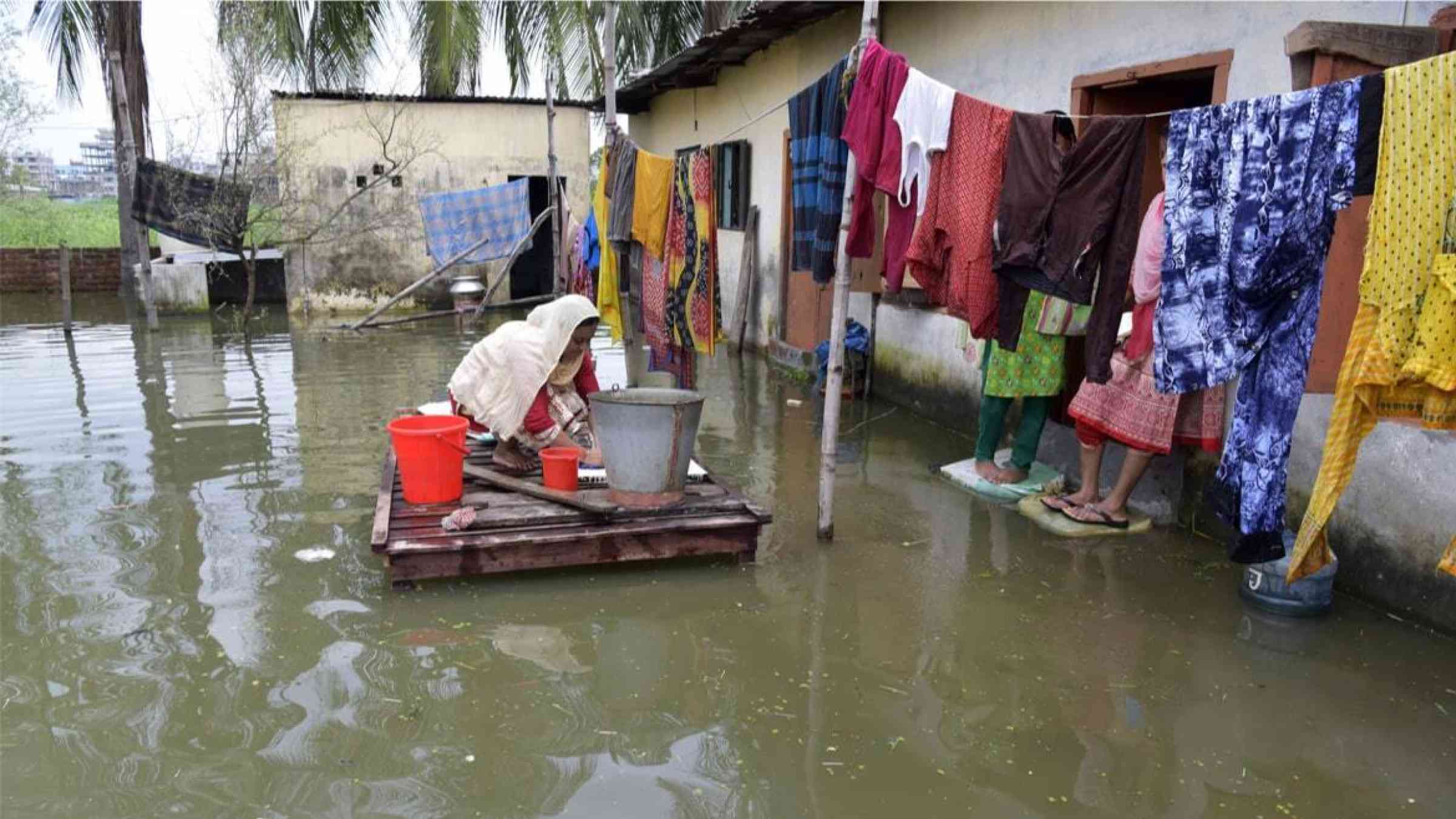 Bangladeshi woman washing clothes in a flooded house