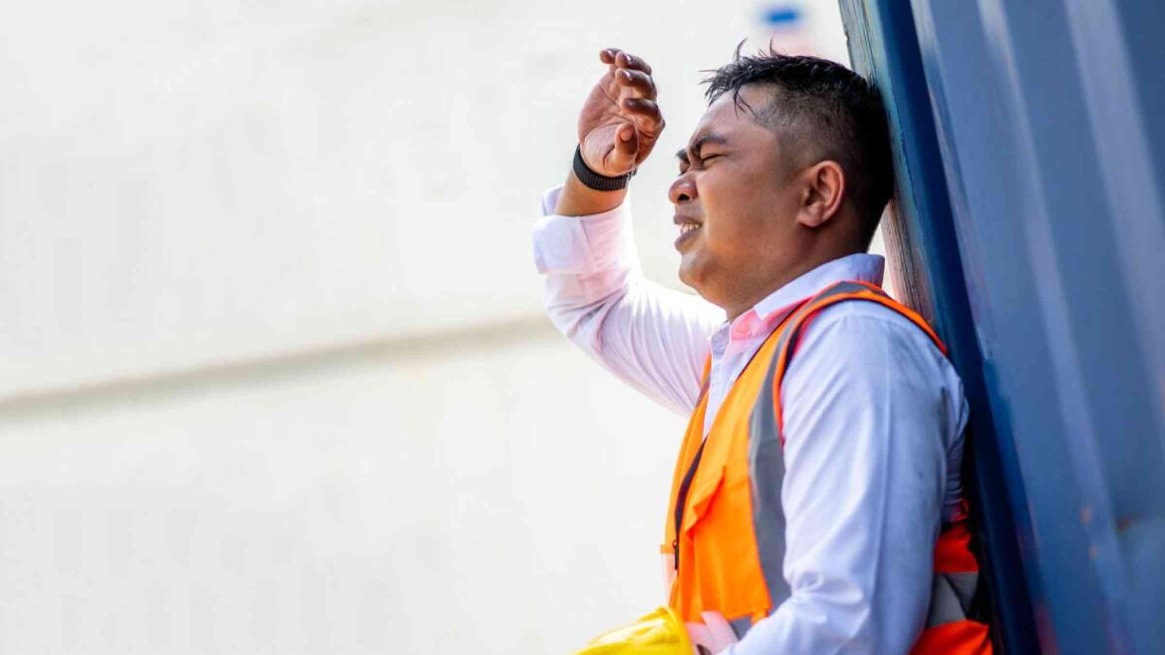 A man in a reflective vest takes a break amidst hot weather