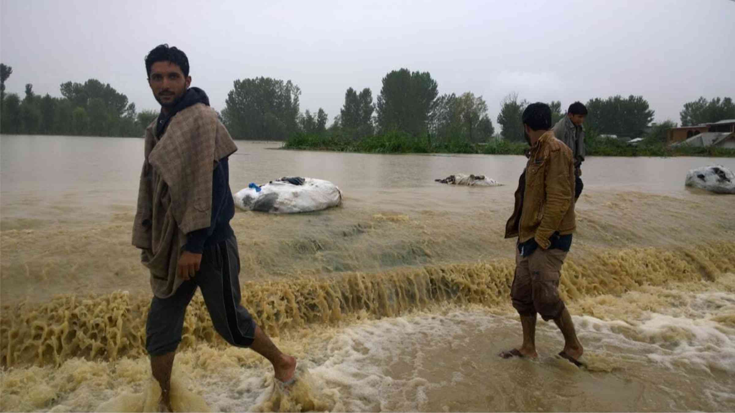 Residents cross a flooded highway in Kashmir