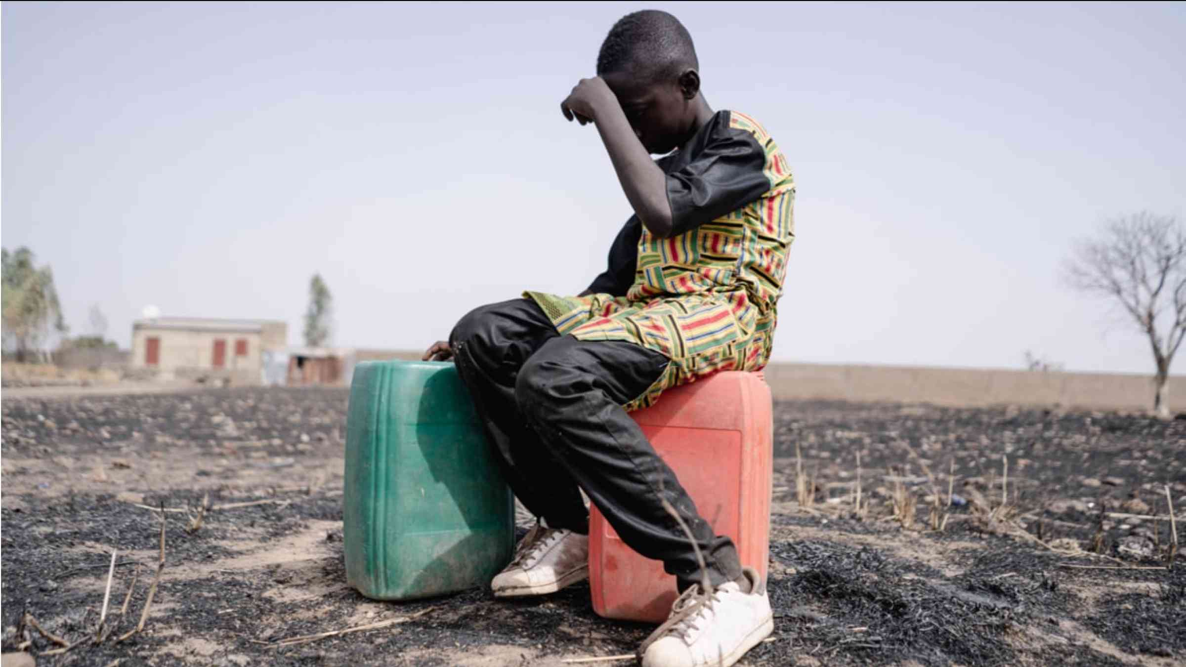 Young African boy sitting in heat on water tanks.